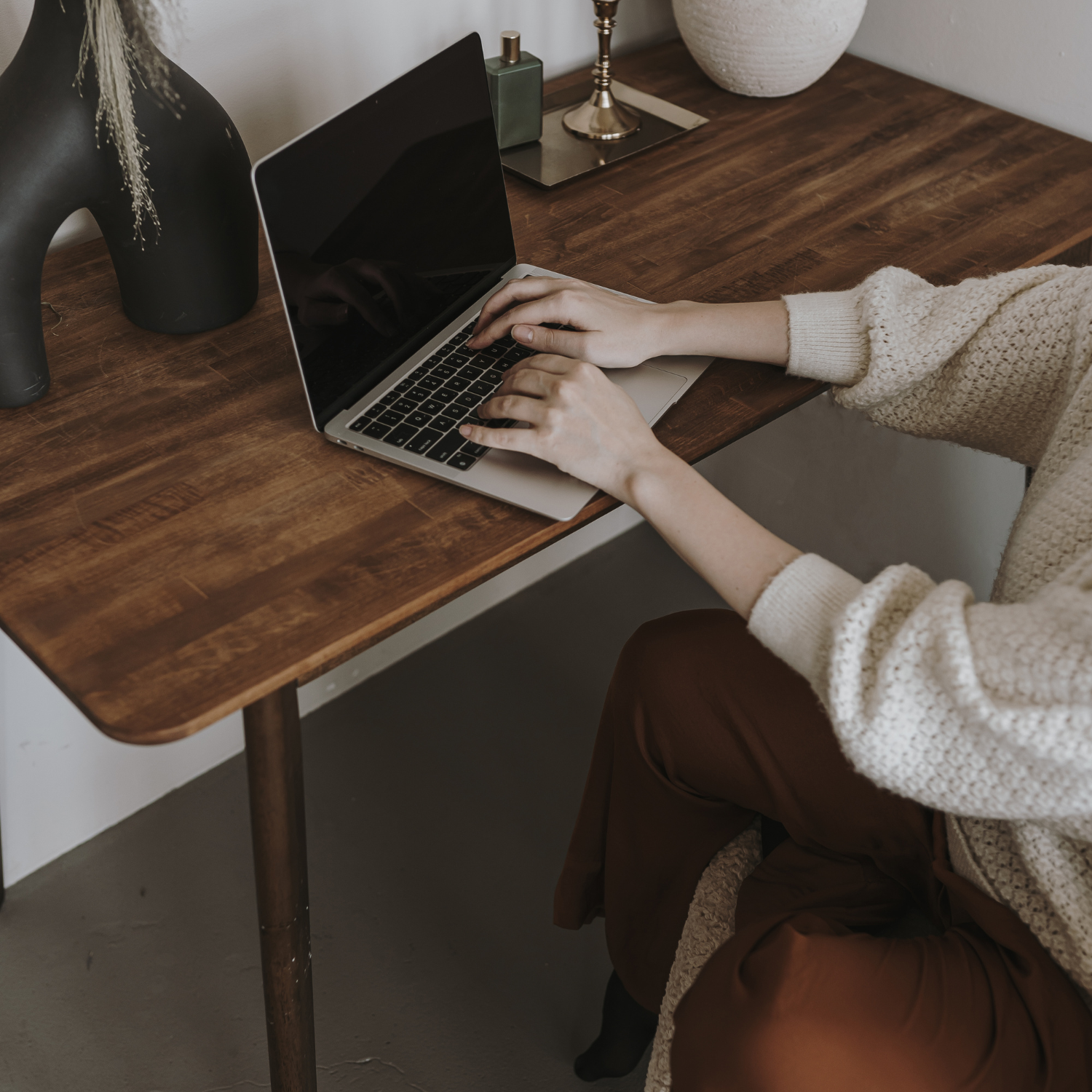 Email Marketing Laws - what you need to know. Photo of woman typing on computer wearing a white sweater. Brown desk with decor.