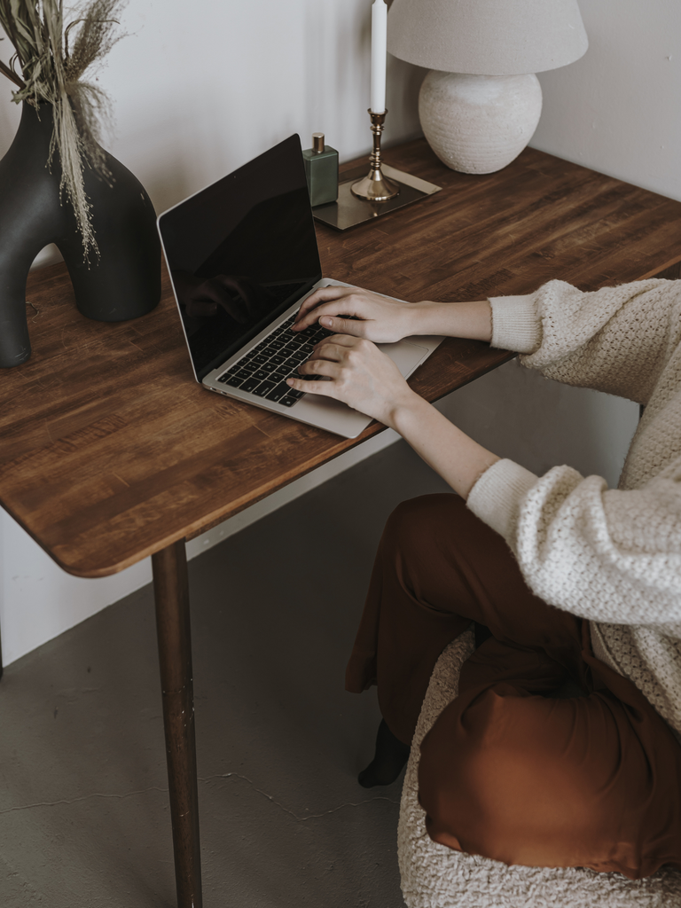 Email Marketing Laws - what you need to know. Photo of woman typing on computer wearing a white sweater. Brown desk with decor.