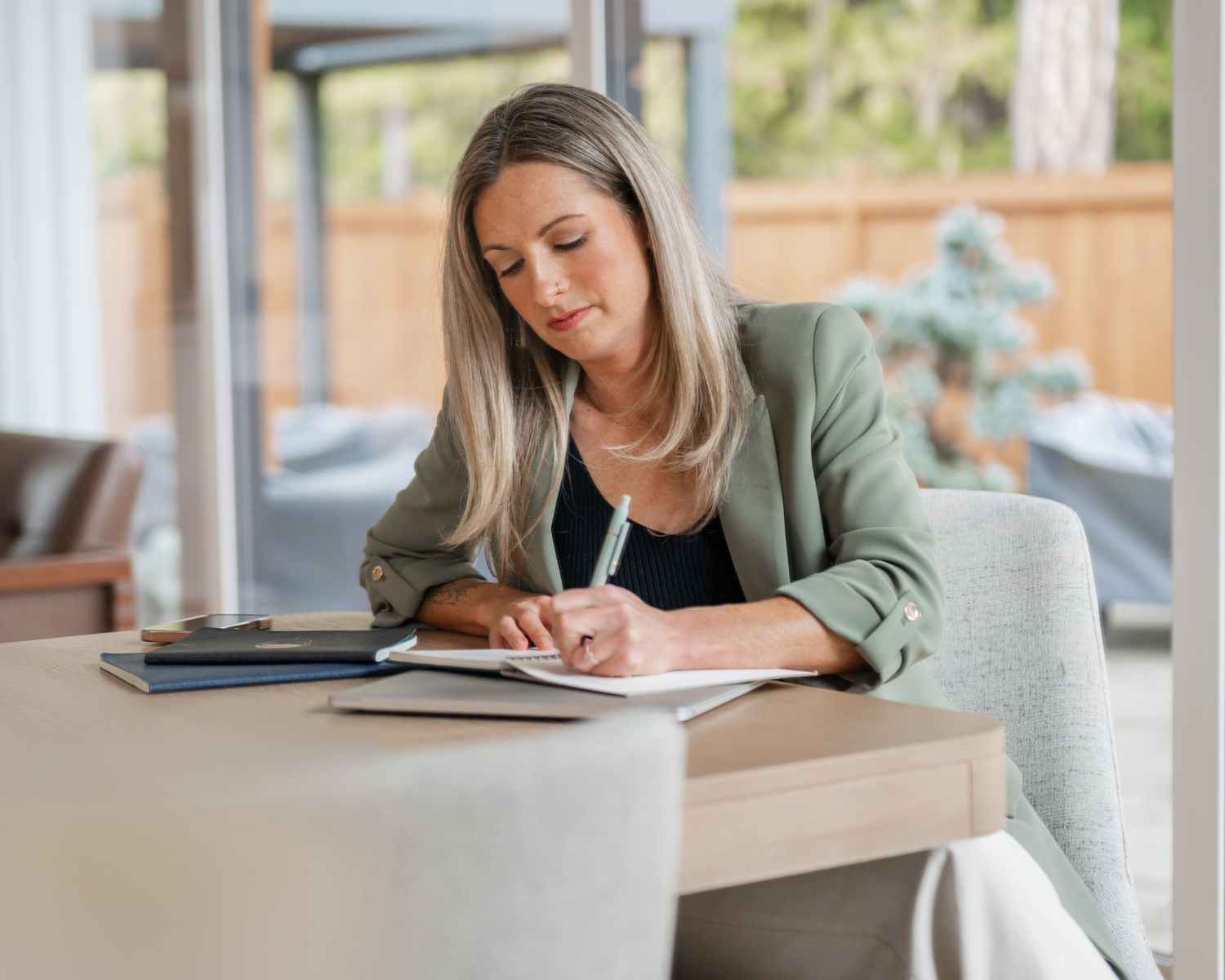 Woman in a green blazer reviewing a coaching contract at a desk by a forest-view window