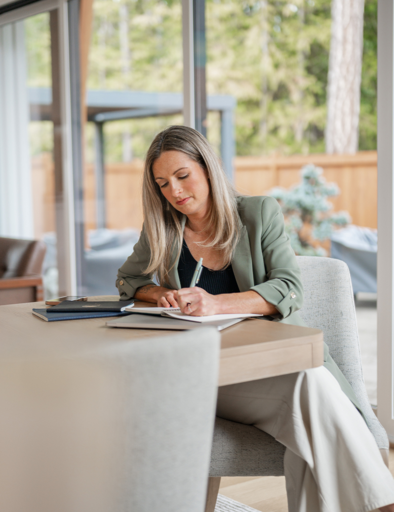 Woman in a green blazer reviewing a coaching contract at a desk by a forest-view window
