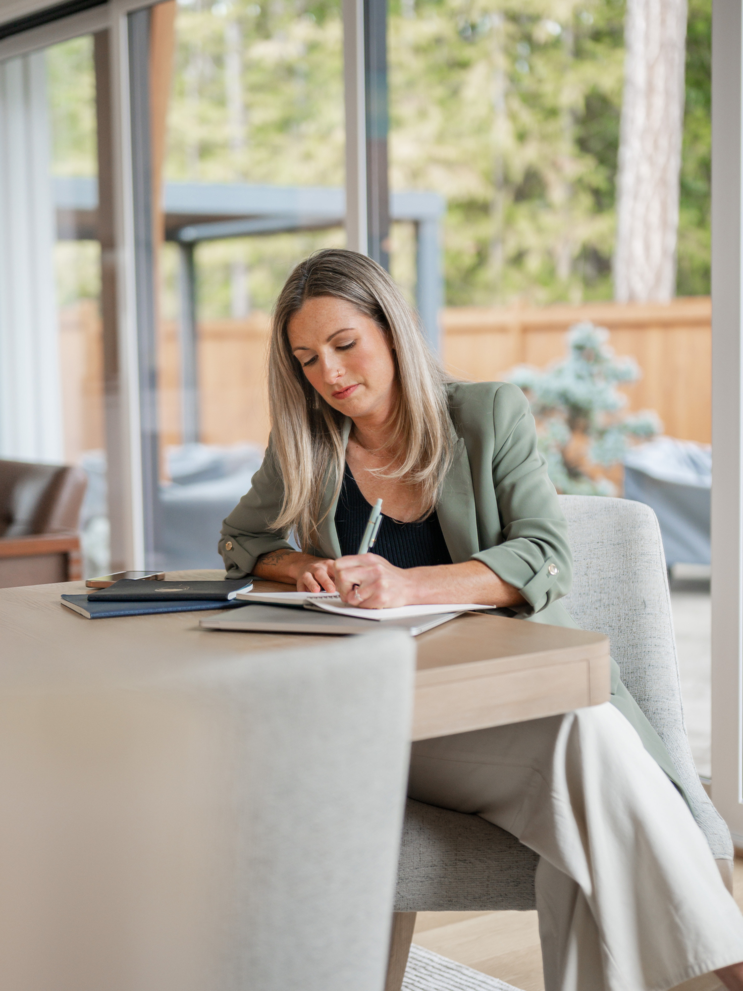 Woman in a green blazer reviewing a coaching contract at a desk by a forest-view window